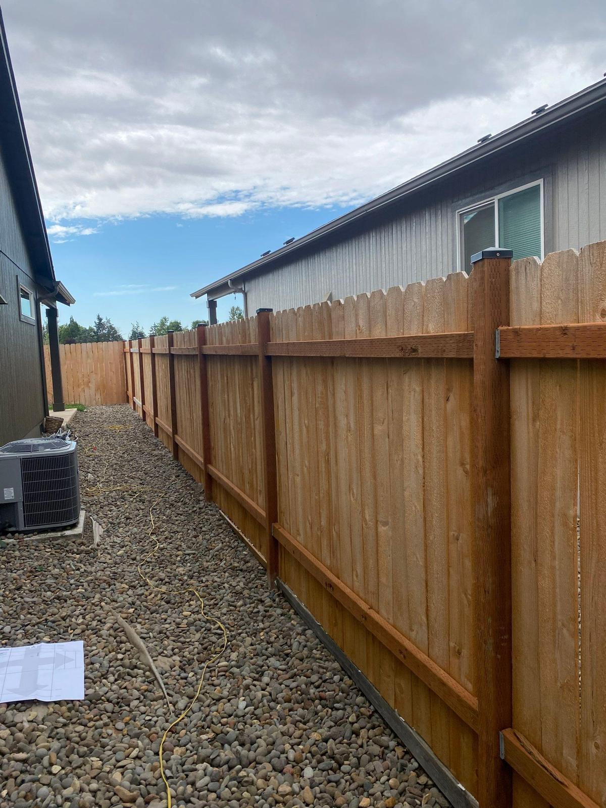 A new cedar privacy fence running the length of a gravel side yard between two houses