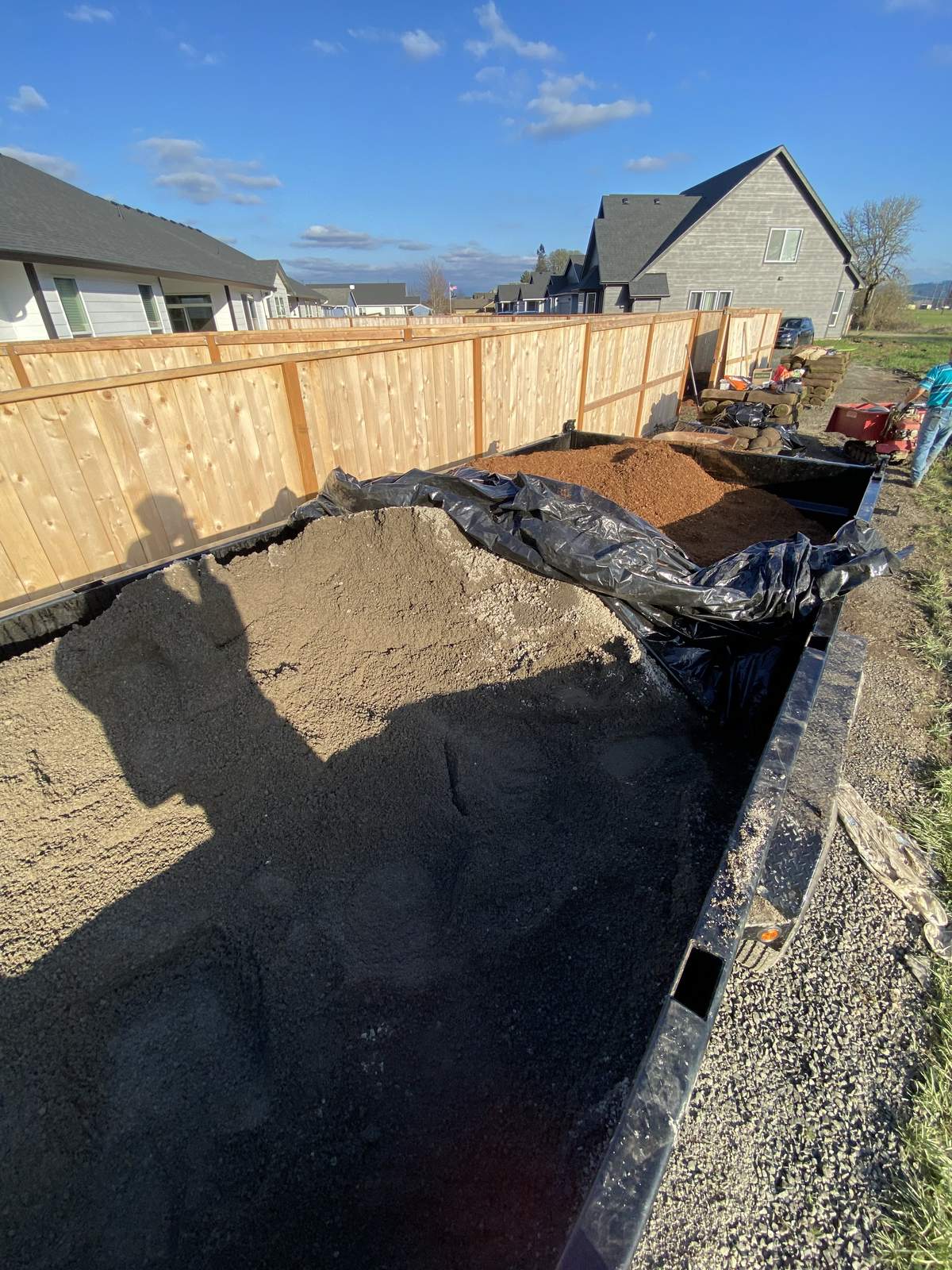 A long dump trailer part loaded with sand and bark standing against a new cedar fence